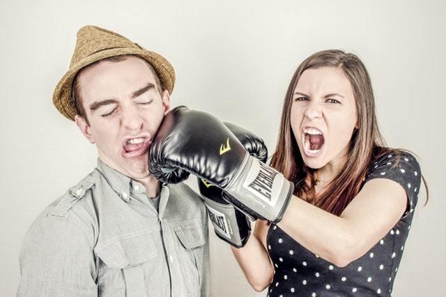 Woman punching a man with a boxing glove in a staged photo, both making exaggerated angry expressions against a plain light background
