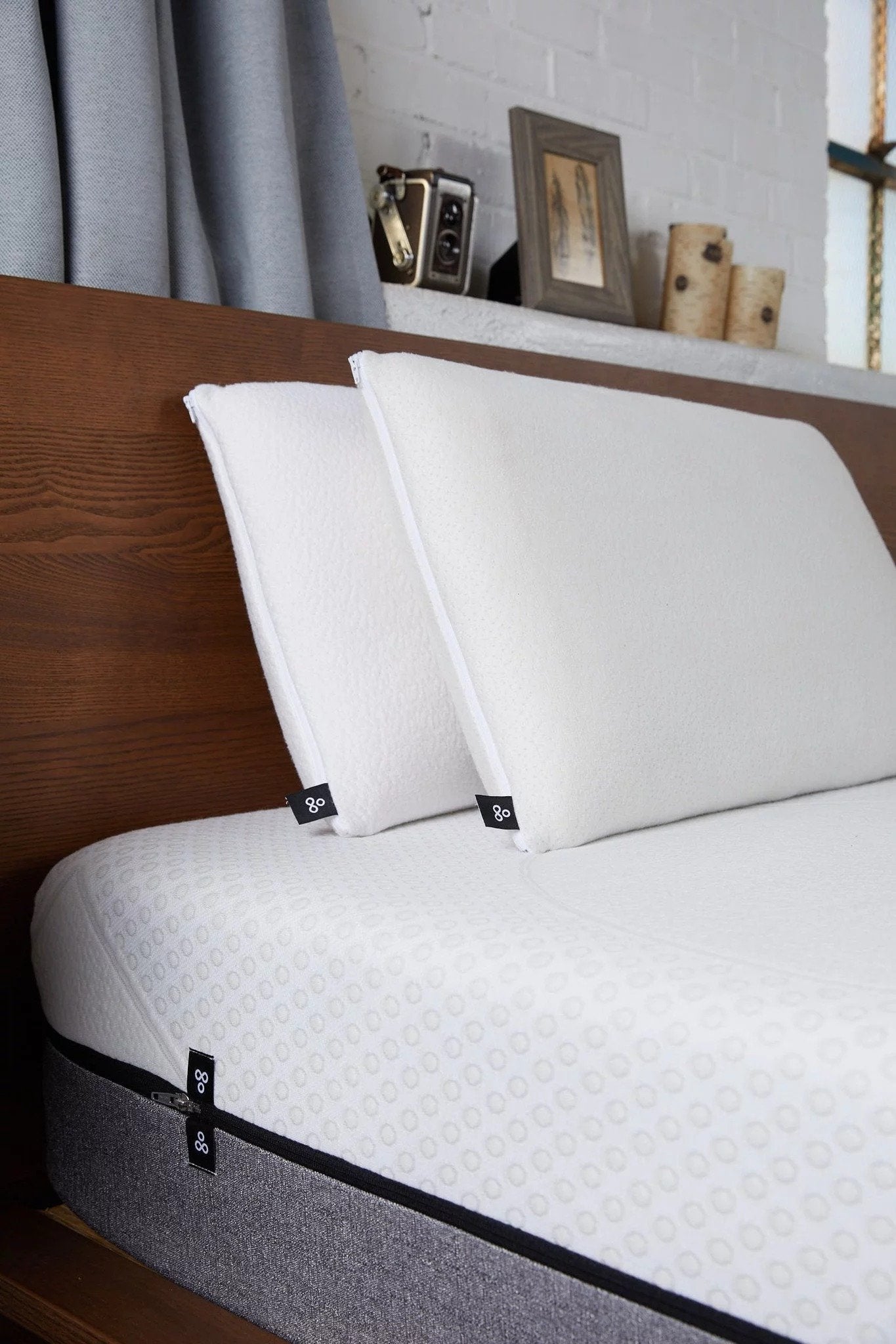 Angled view of two white pillows propped against a wooden headboard showing textured removable covers and upright support