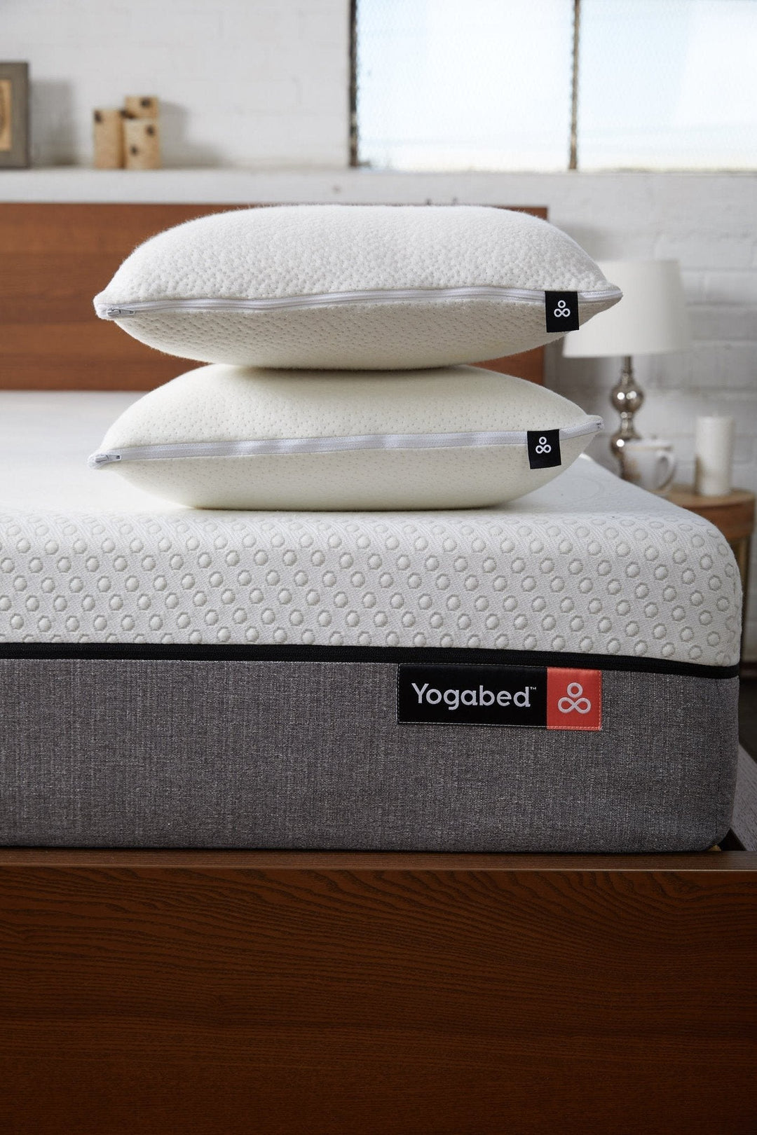 Side view of two stacked white pillows with zippered removable covers and textured knit surface on a mattress in a bedroom