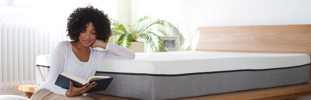 Woman leaning against a mattress reading a book in a bright bedroom