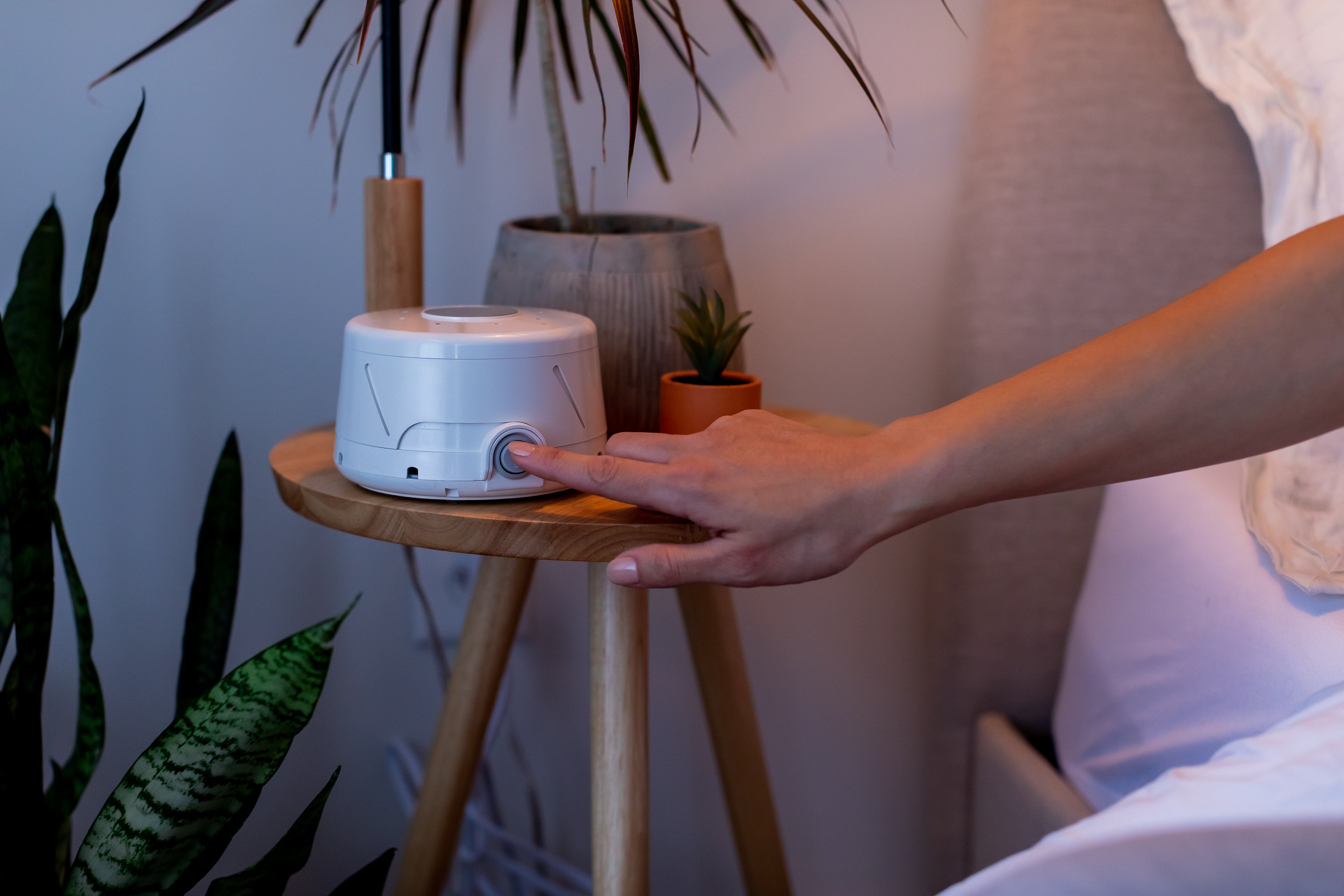 Front view of Yogasleep white noise machine with a finger pressing its power knob on a bedside table
