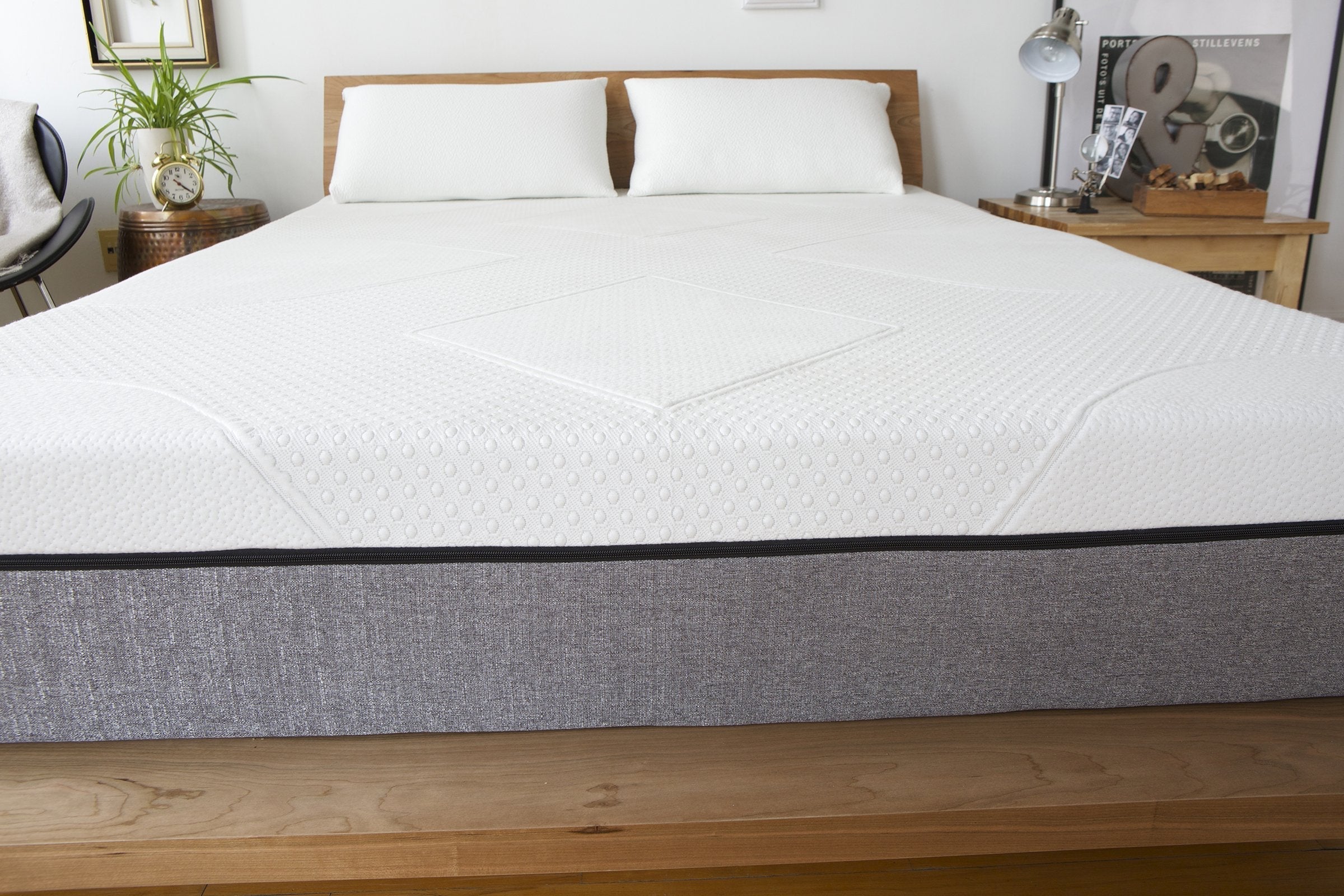 Front view of mattress on wooden platform showcasing textured white quilted cover and gray fabric base in a bedroom setting