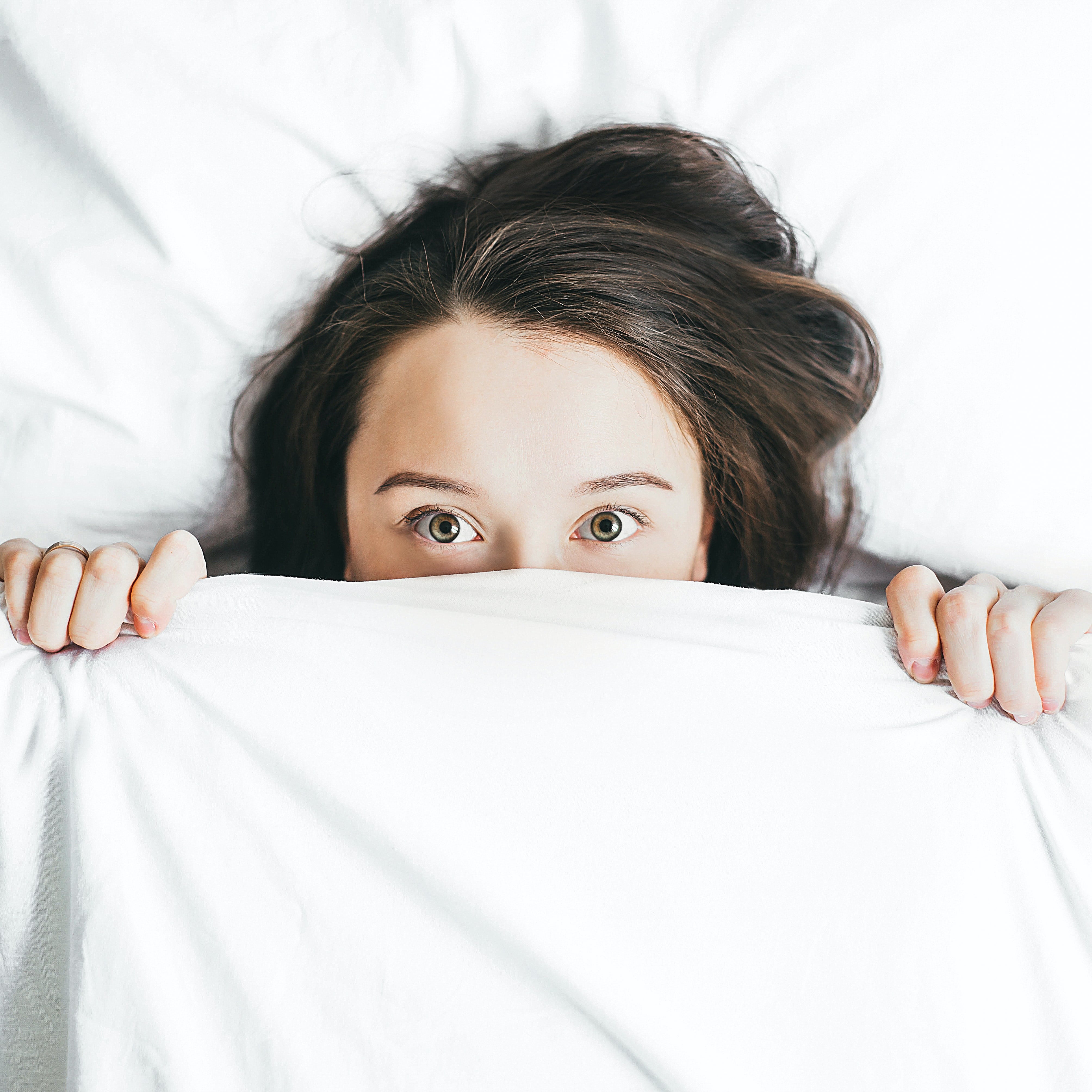 Person peeking over a white duvet in bed, wide-eyed and restless