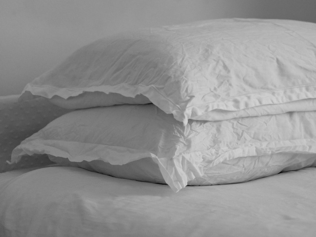 Side view of stacked white pillows showing soft, wrinkled cotton covers and ruffled edges on a plain bed background