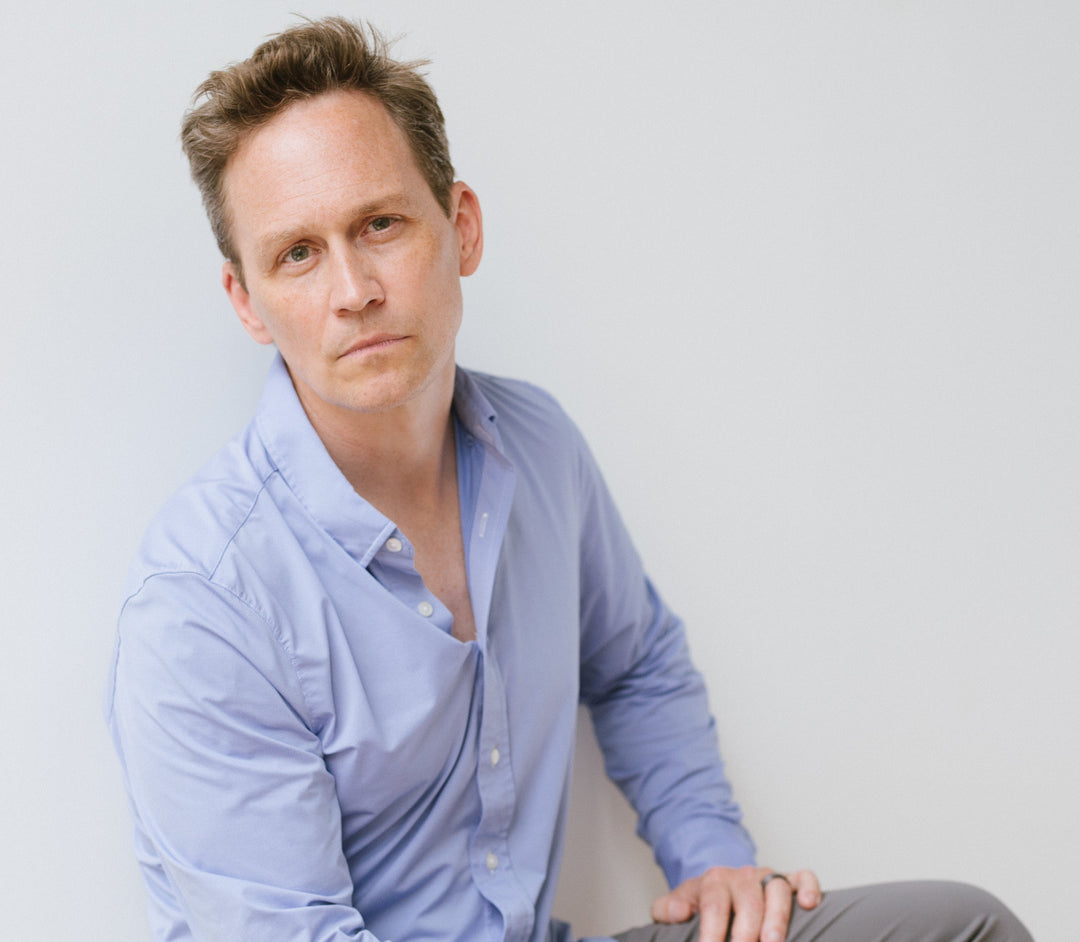 Man in a light blue button-down shirt looking at camera against a plain pale gray background