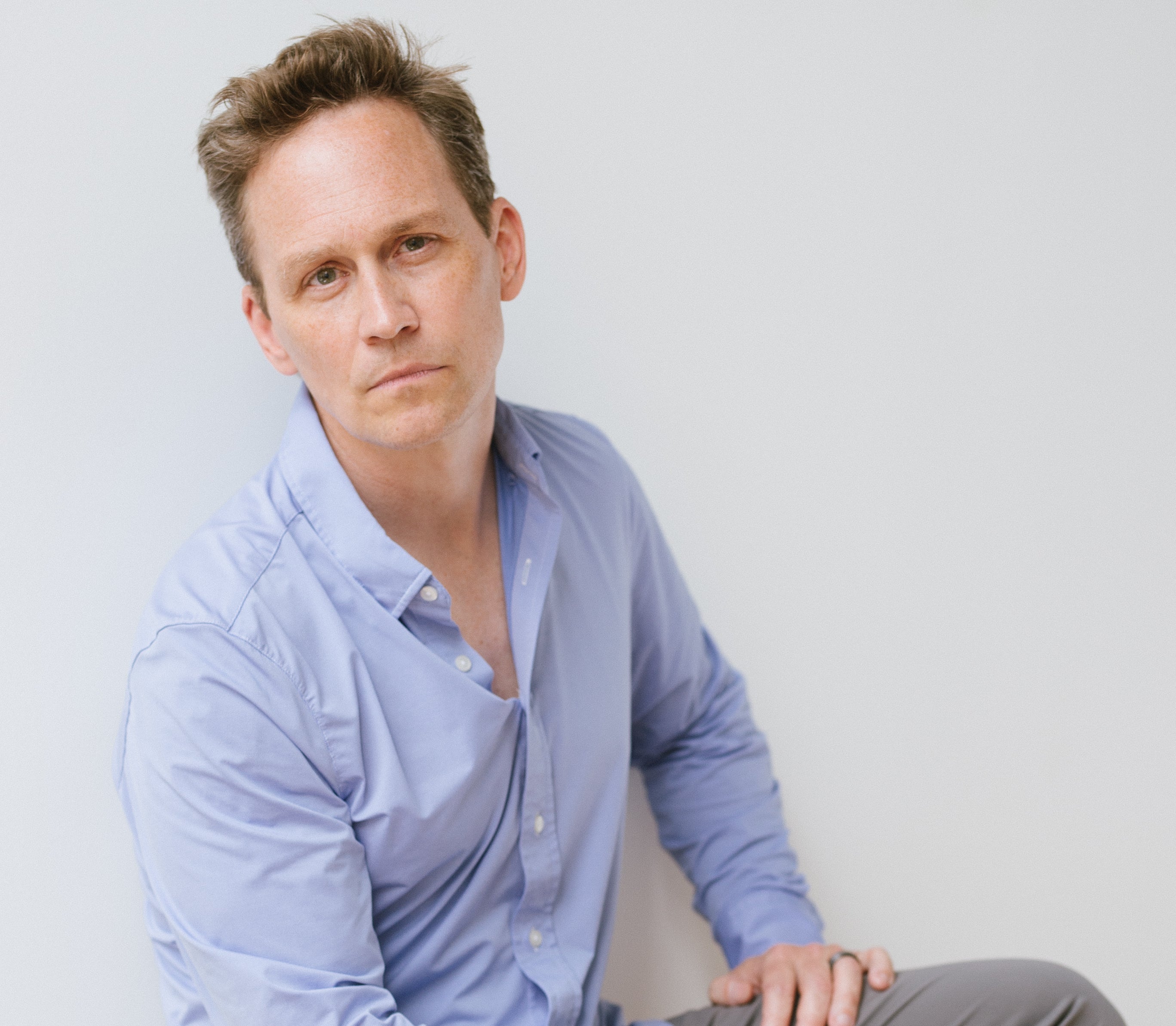 Man in a light blue button-down shirt looking at camera against a plain pale gray background