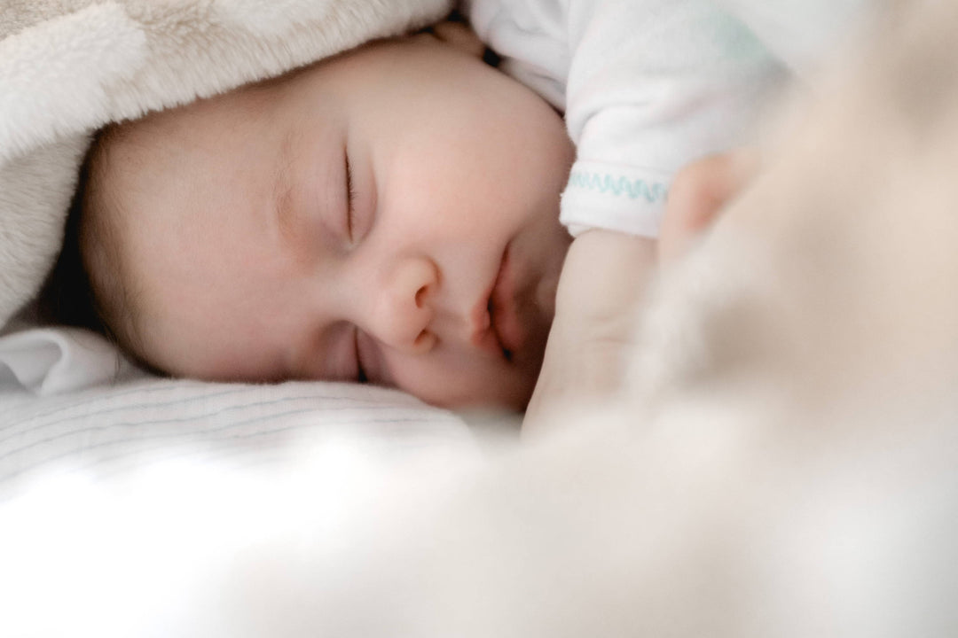 Newborn baby sleeping, curled under a soft blanket in a close-up shot
