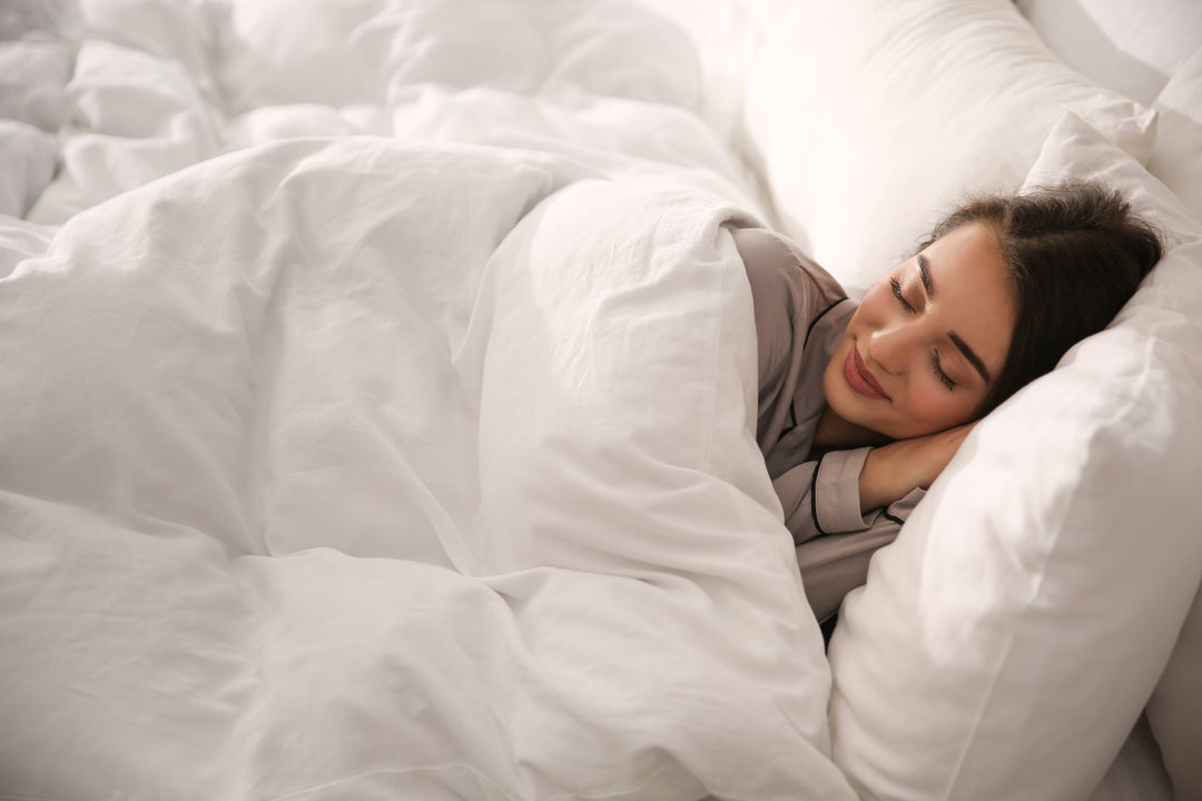 Woman sleeping on her side in bright white bedding with her head on a pillow, looking relaxed