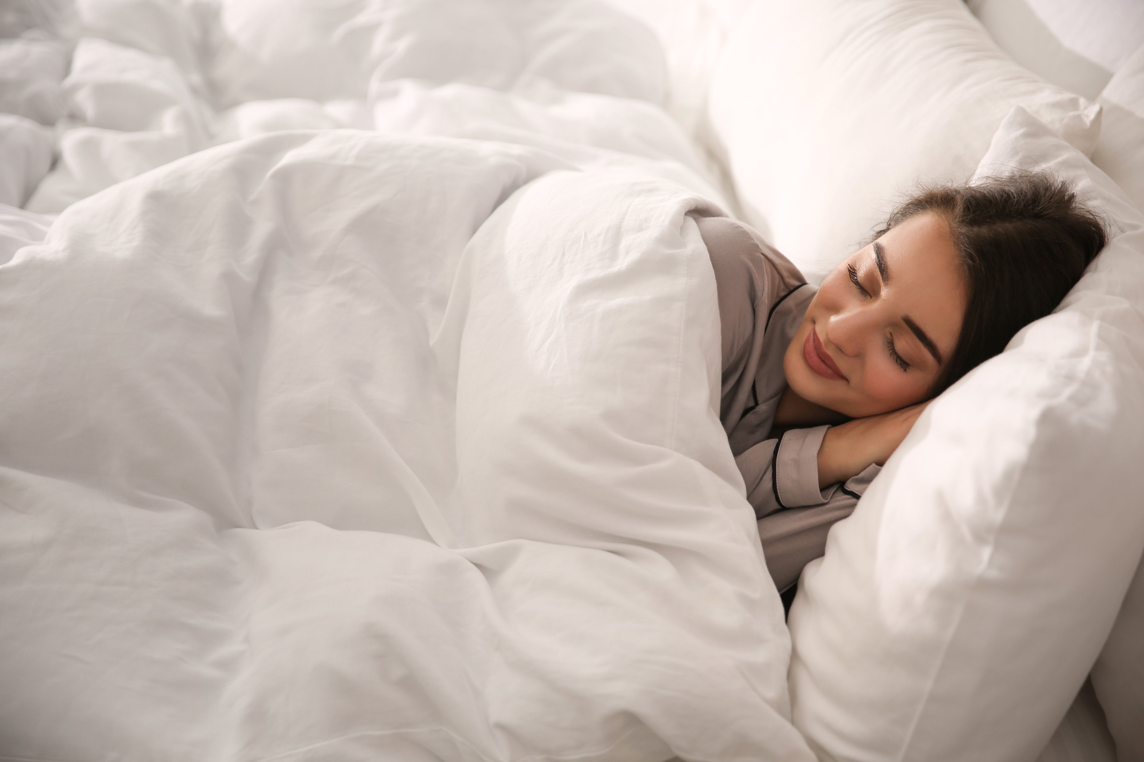 Woman sleeping on her side in bright white bedding with her head on a pillow, looking relaxed