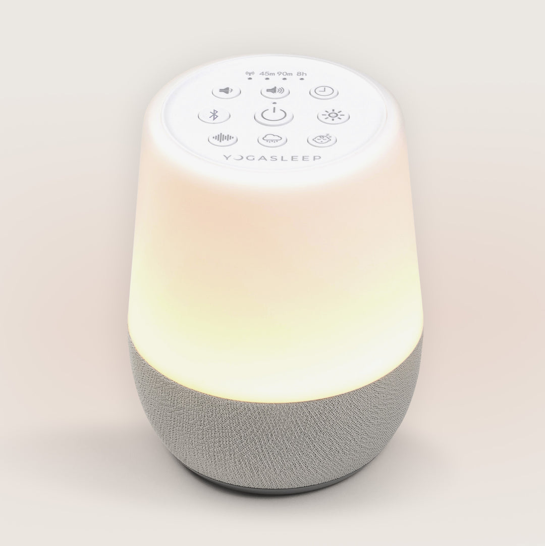Top-down angled view of Hushh 2 sound machine with warm glowing nightlight, visible top buttons, and gray fabric speaker base