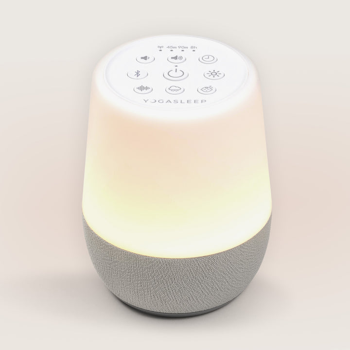 Top-down angled view of Hushh 2 sound machine with warm glowing nightlight, visible top buttons, and gray fabric speaker base