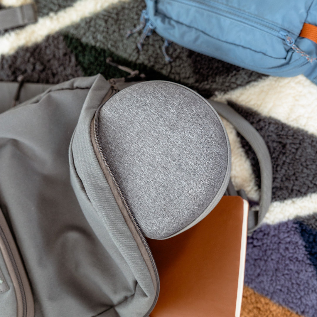 Dohm travel case tucked into a gray backpack pocket on a patterned rug, showing portability for travel
