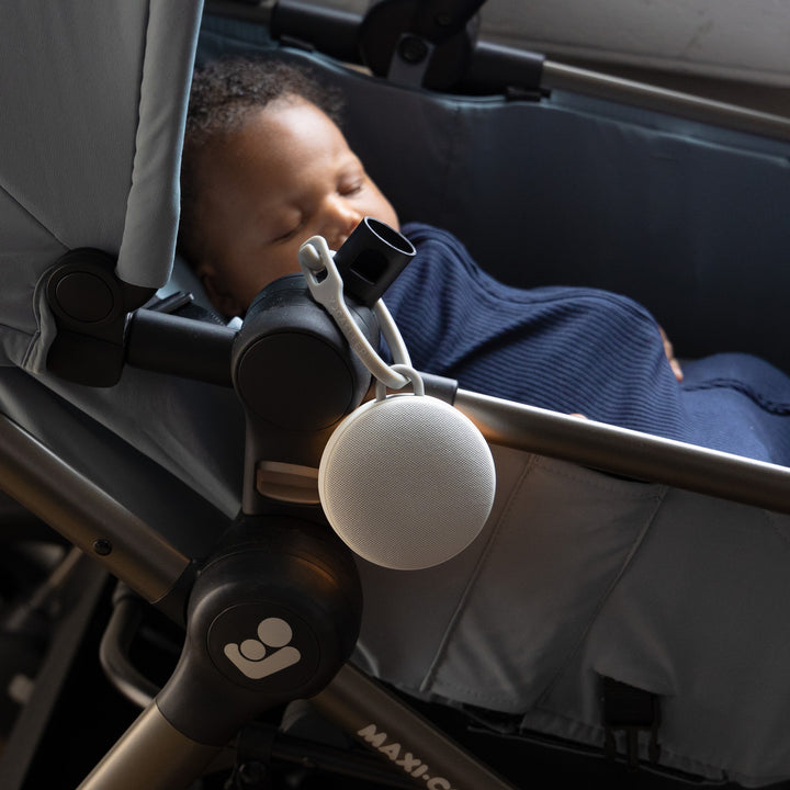 Infant sleeping in a stroller with a white Hushh 2 travel sound machine clipped to the stroller frame