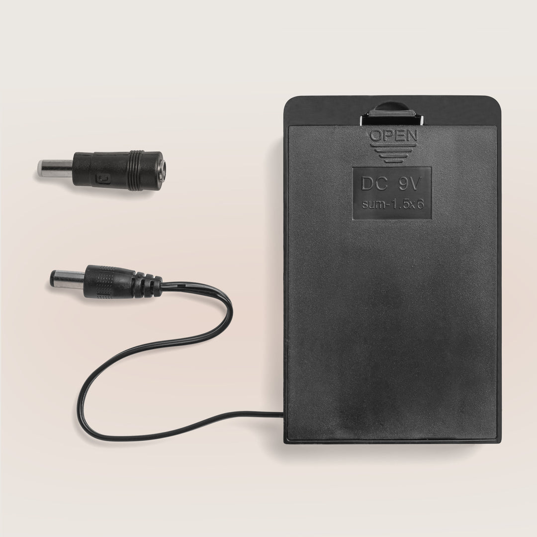 Top-down view of Marsona Battery Backup showcasing a black battery pack with attached cable and two DC adapter plugs on a light beige background