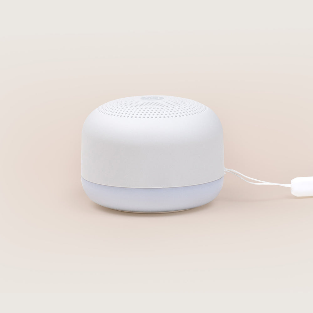 Front view of Travel Mini sound machine showcasing white casing, perforated speaker top and illuminated night-light base on a beige background