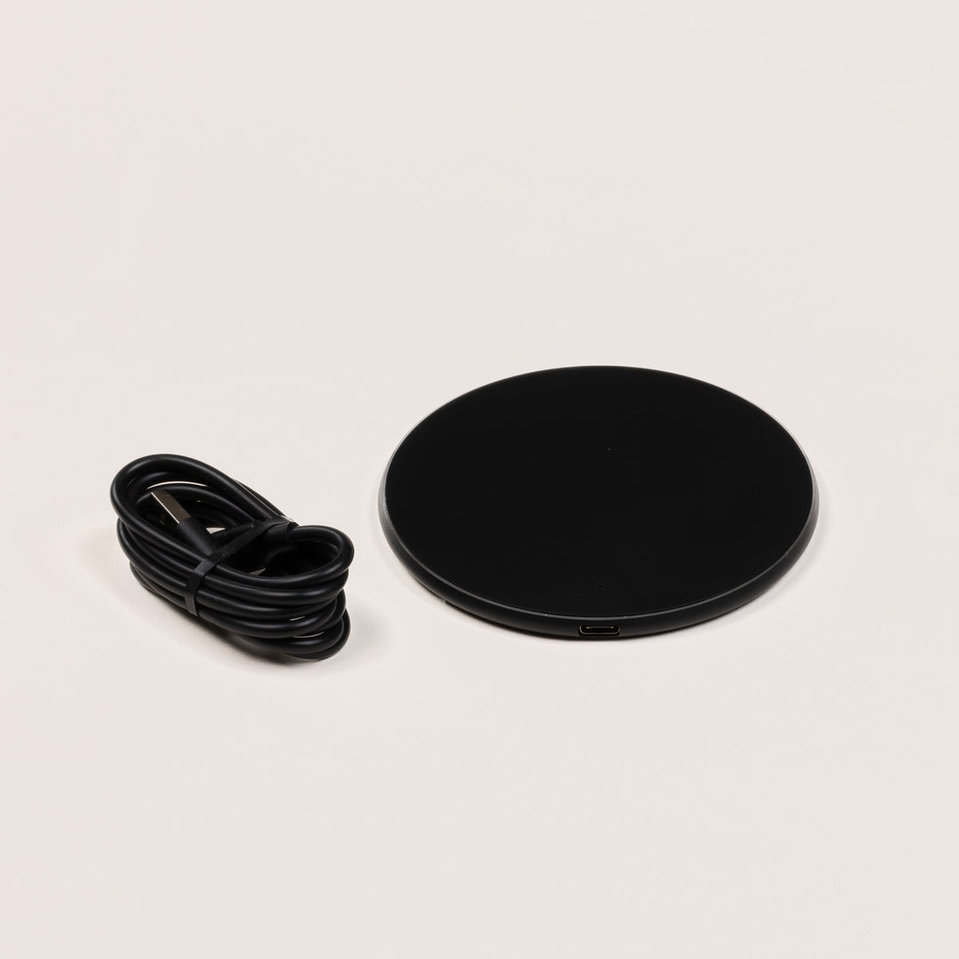 Top-down view of Wireless Charging Pad showing round black surface, silver edge, LED, and cable on a beige background