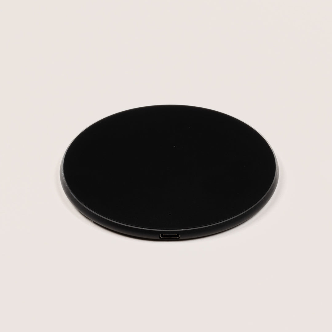 Angled view of Wireless Charging Pad showcasing black charging surface, silver edge and small LED indicator on a beige background