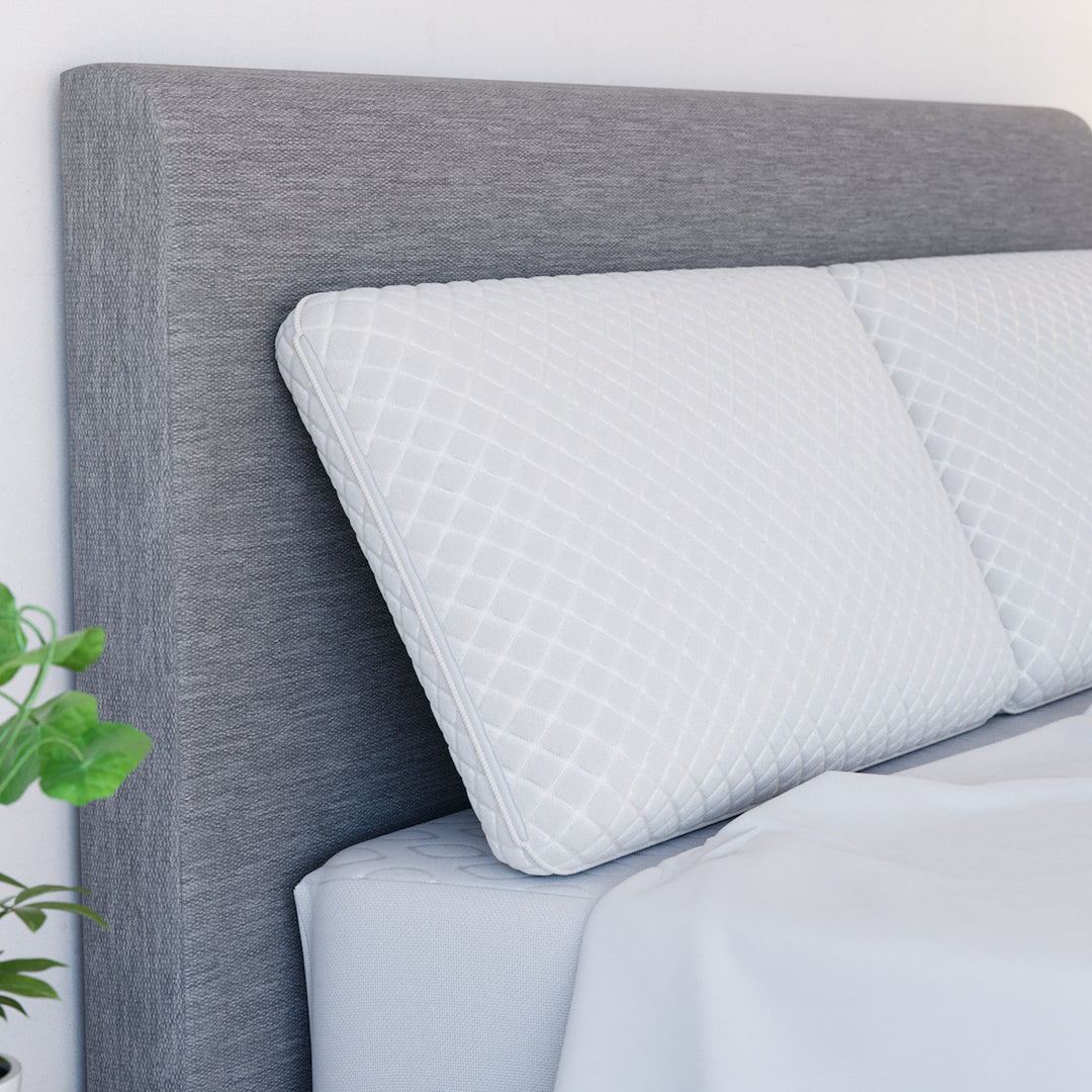 Angled view of Yogabed Essential Sleep Bundle sheet set with pillows showcasing white bedding against a gray upholstered headboard