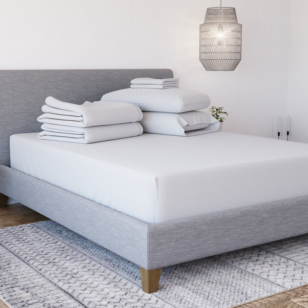 Front three-quarter view of Yogabed Essential Sleep Bundle showcasing white bedding and pillows on a gray upholstered bed