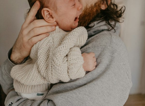Bearded father gently cradling and soothing a crying infant wearing a knit sweater