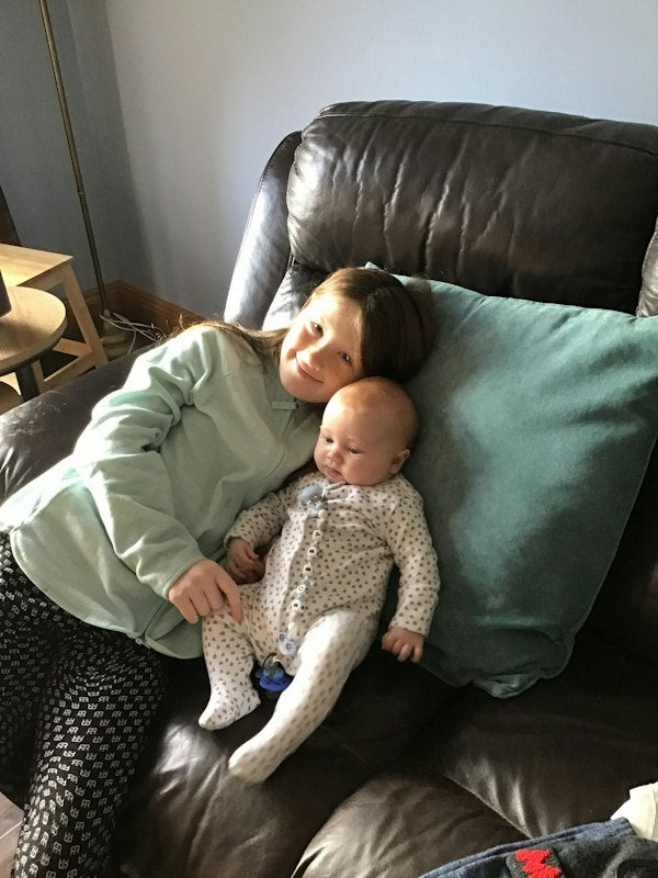 Young girl smiling while cuddling her baby sibling on a brown leather armchair