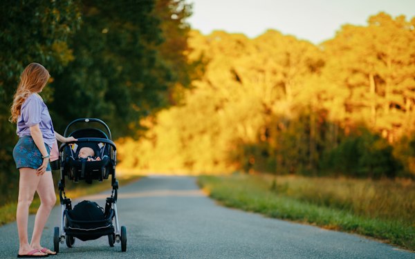 Mother pushing a baby stroller along a country road during golden hour sunset