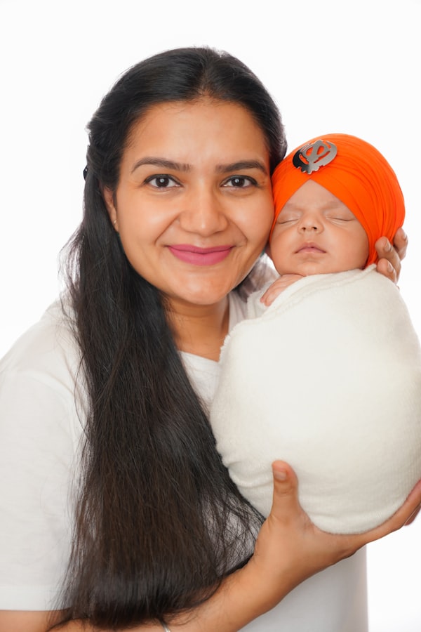 Smiling mother holding her swaddled newborn wearing an orange turban with a Khanda emblem