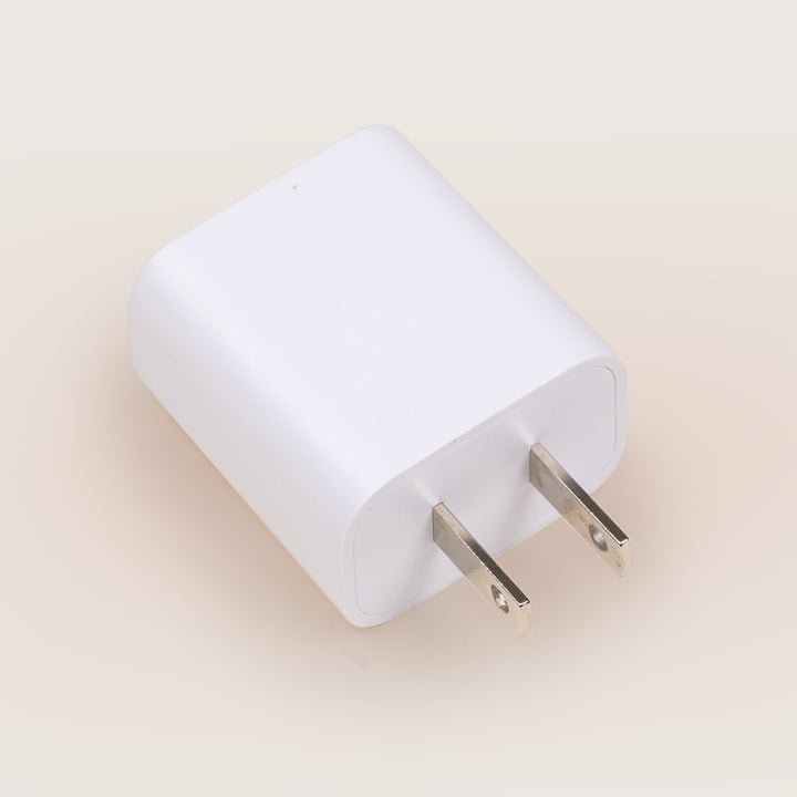 Angled top view of white USB power adapter showing two flat US prongs on a pale beige background