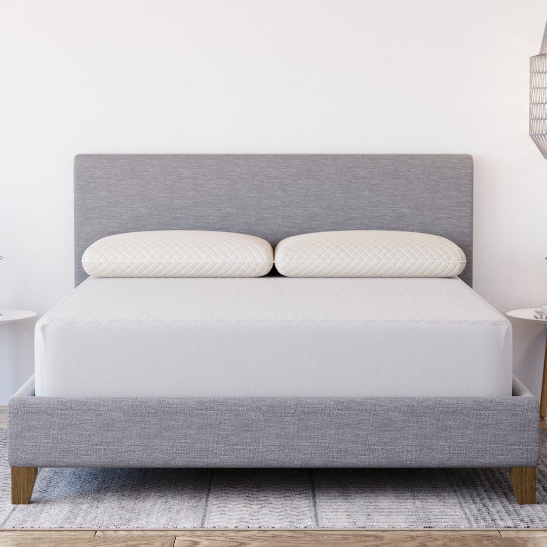 Front view of Yogabed Ultra Cool Waterproof Mattress Protector showcasing fitted coverage on a bed with gray upholstered headboard