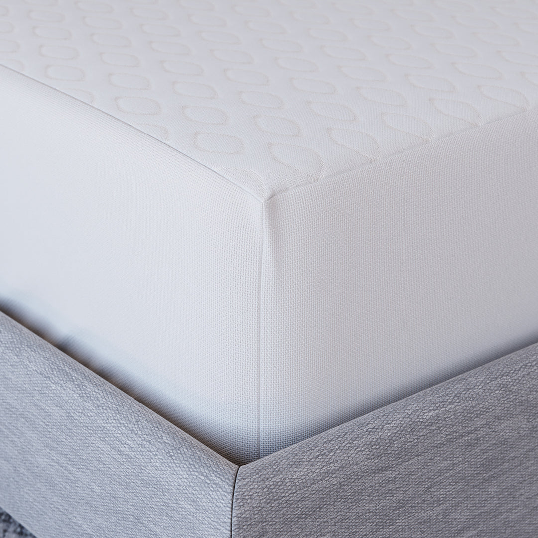 Close-up corner view of Yogabed Ultra Cool Waterproof Mattress Protector showcasing the fitted waterproof cover on a gray bed base