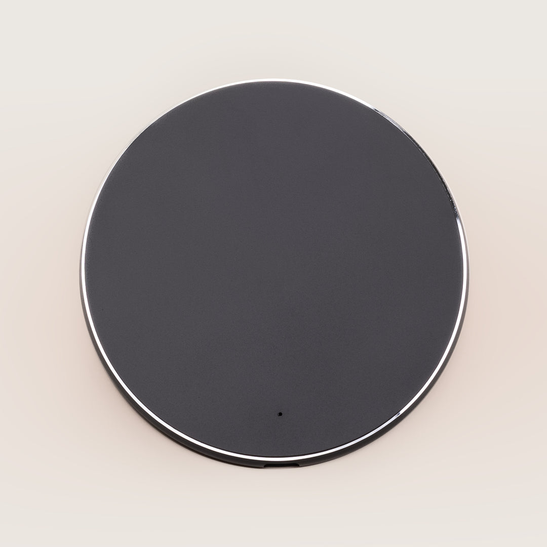 Top-down view of Wireless Charging Pad showing round black surface with silver edge and small LED on a neutral beige background